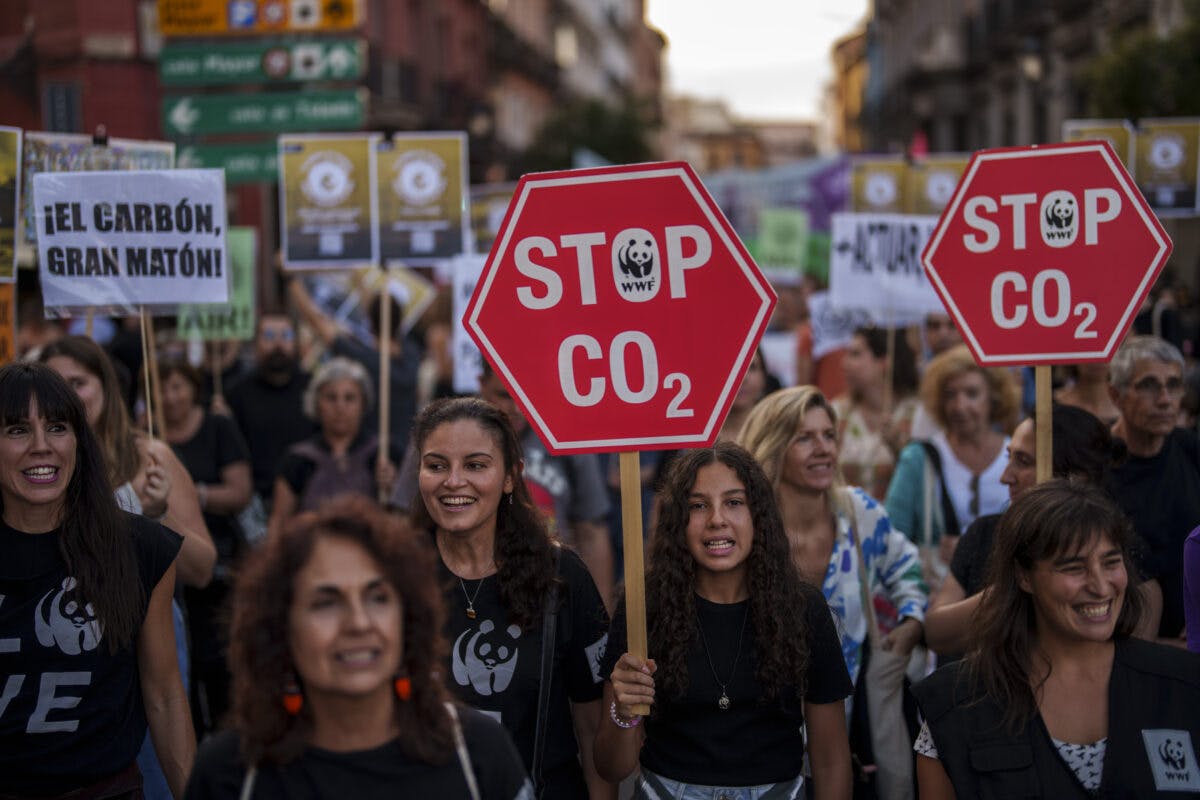 Demonstranter bærer "stopp co2"-skilt ved en demonstrasjon av klimaendringer, med mennesker i forskjellige aldre som smiler og går i en bygate.