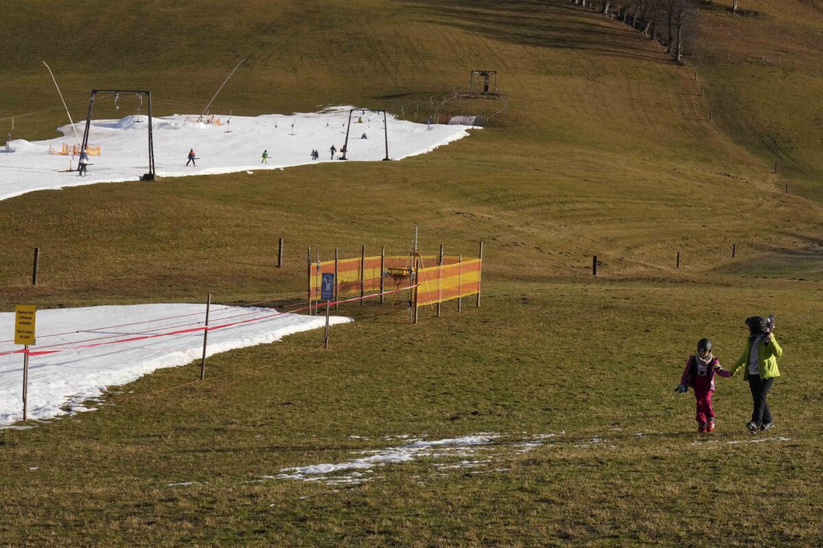 Mennesker står på grønt gress ved skianlegg.